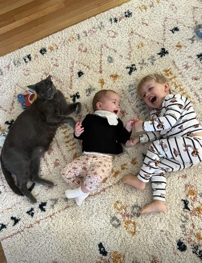 Bruce the cat, Ollie, and the baby lying on a carpet beside one another